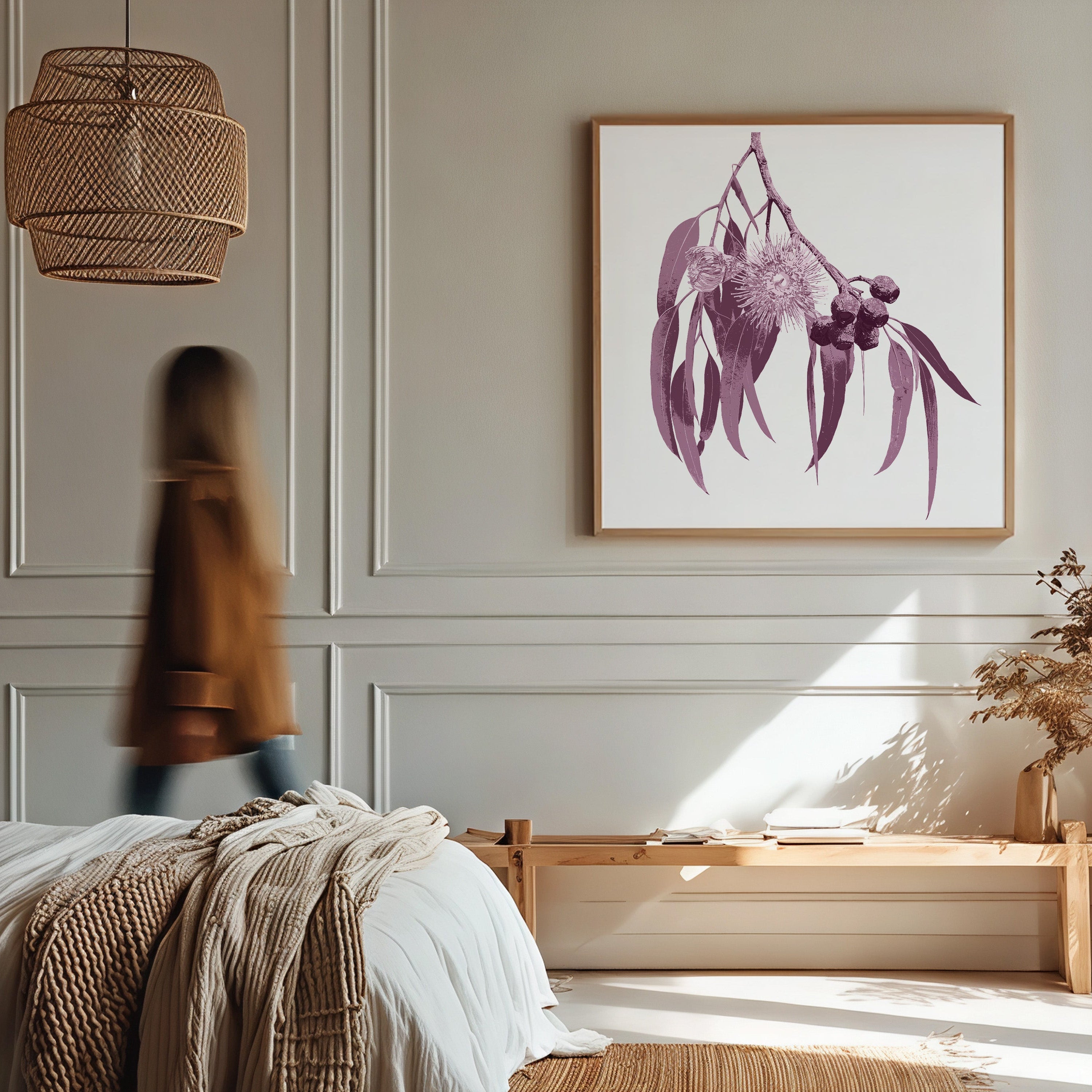 Modern bedroom with a person walking by, framed artwork on the wall, and a vase with dried plants.